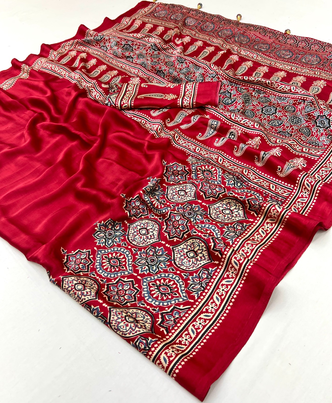 Red Ajrakh Satin Silk Saree in premium Modal Satin Silk with elegant digital print, tassels on pallu, 6.3 meter saree with matching blouse piece for festive and party wear.